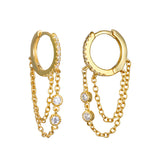 A pair of gold huggie hoop earrings with small clear crystals and draped double chains holding two round stones.