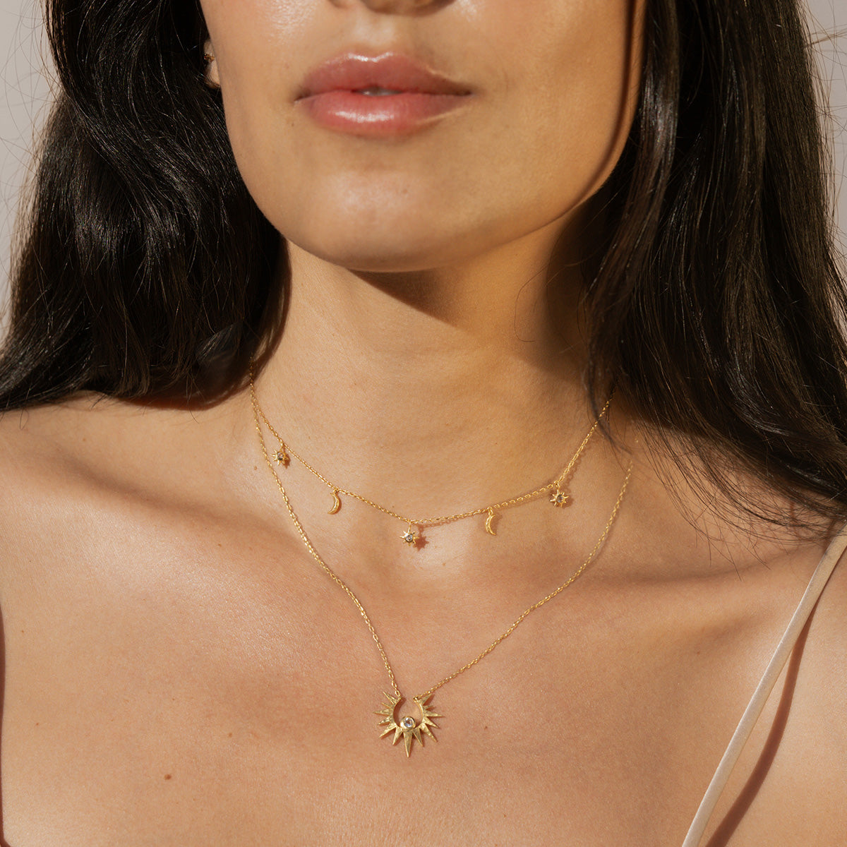 Two-layered gold necklaces with crescent moon, star, and sun charm pendants worn on model.