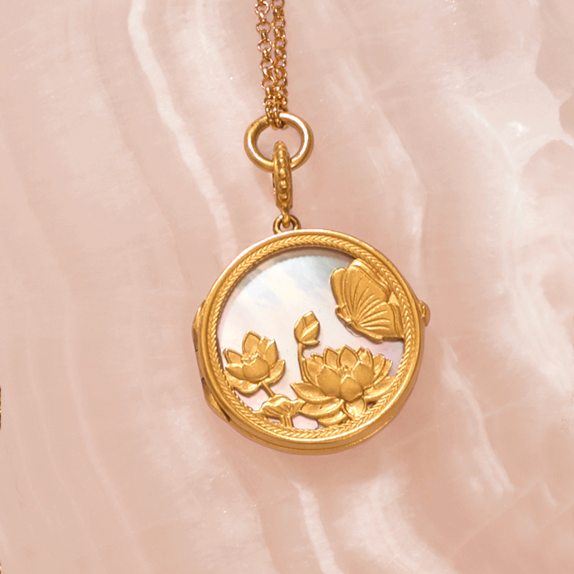 Gold-toned circular locket pendant with mother-of-pearl center, featuring embossed lotus flowers and butterfly, hanging from 