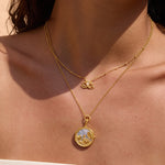 Gold-toned layered necklaces worn on skin, featuring a butterfly pendant and circular locket pendant with visible interior de