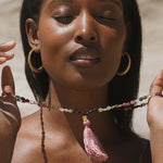 A woman peacefully displays the Peaceful Spirit Tourmaline Gemstone Mala, surrounded by soft sunlight, embodying the essence of spiritual jewelry and meditation. This mala serves as a talisman for zodiac signs, enhancing protection and meaningful manifestations during yoga practices.