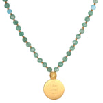 Green and blue faceted beads strung with gold spacers and a gold pendant engraved with text.