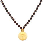 Mala necklace with dark red faceted beads separated by gold spacers, featuring a gold circular pendant engraved with "I am gr