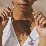 Beaded mala necklace with black and cream stones, gold spacers, and gold pendant charm worn around neck.