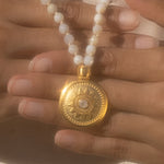 A detailed view of the sun pendant on the Tranquil Dawn White Opal Sun Mala, with white opal beads surrounding it, representing protection and spiritual meaning in yoga and meditation.