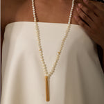 Cream beaded mala necklace with mother of pearl spheres and gold tassel pendant worn over white garment.