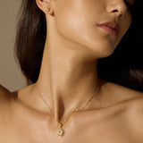 A woman with long dark hair wears a gold starburst pendant necklace with a pale stone and a matching stud earring.