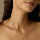 A woman wears a delicate gold chain necklace with a small sunburst pendant set with a clear pale stone.