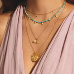 Dazzling Mother Moon Gold Locket Necklace showcased with layered spiritual jewelry against a soft pink background, embodying themes of meditation, protection, and meaningful charm for zodiac enthusiasts and yoga practitioners.