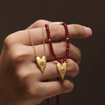 Close-up image of two Healing Heart Red Onyx Heart Necklaces held in a hand, emphasizing the gold heart pendant and red onyx beads. This spiritual jewelry serves as a talisman for meaningful practices like meditation and manifestation.