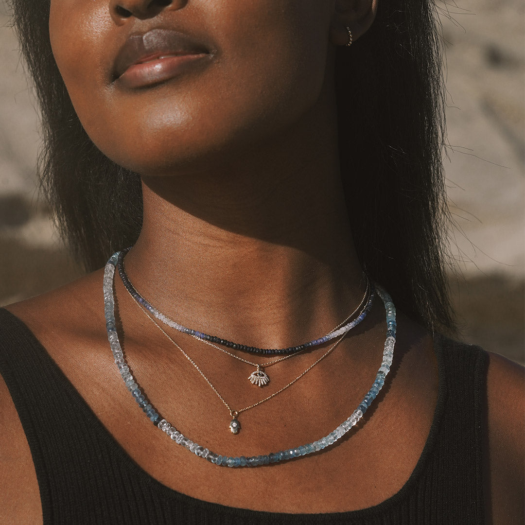 Person wearing the Shades of Courage 14kt Gold Aquamarine Necklace layered with other spiritual jewelry, showcasing an elegant style that promotes meditation, meaning, and manifestation. This stunning piece acts as a talisman for courage, complementing the energies of the zodiac with protection and peace.