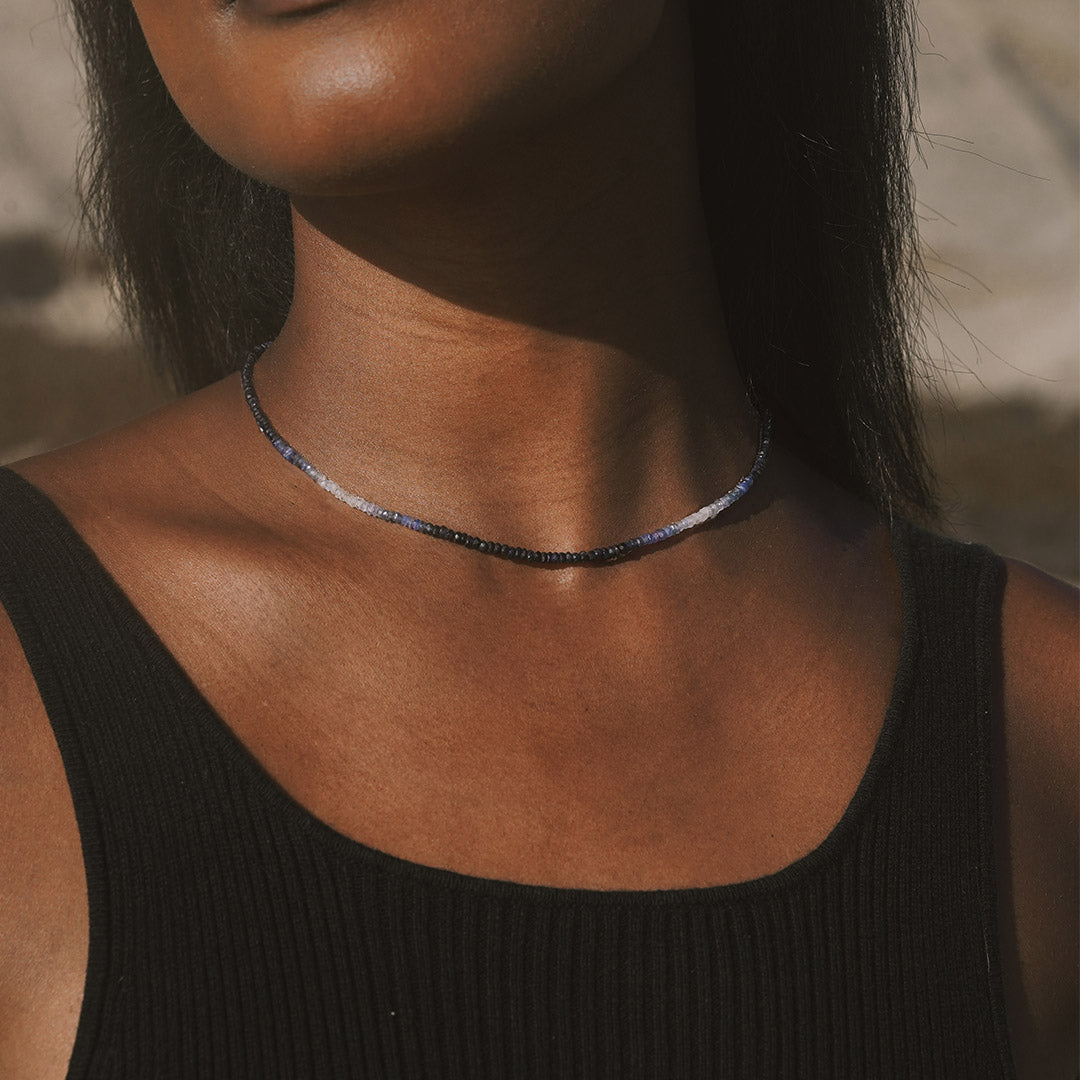 A model wearing the Shades of Love 14kt Gold Sapphire Necklace, highlighting the beautiful shades of sapphire against the skin. This necklace represents spiritual and meaningful adornment, ideal for those who seek protection and harmony in their daily lives, connecting with the energies of the sun and moon.