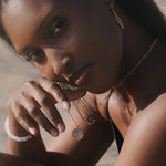 A close-up shot of a woman elegantly showcasing the Shine in Sisterhood Constellation Necklace, which symbolizes spiritual connection and empowerment. The necklace features a gold-plated pendant adorned with seven pyrite stars, representing reflection and prosperity. This piece of spiritual jewelry is perfect for those who embrace meditation and seek meaningful talismans for protection and manifestation, complementing practices like yoga and connecting with the energies of the sun and moon.