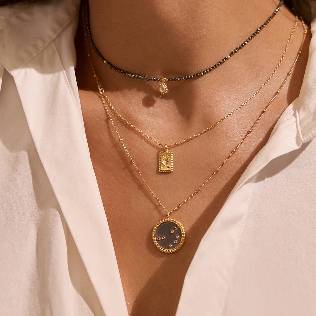 Stylish layered necklaces including the Dreams of Prosperity Pyrite Necklace, showcasing elegance through spirituality. The combination of various necklaces highlights the essence of spiritual adornment, captivating both yoga practitioners and those seeking meaningful talismans for protection and manifestation. Emphasizing the sun and moon theme, this look is ideal for meditation and zodiac lovers.