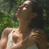 Gold lariat necklace with lotus pendant worn on woman's chest outdoors.