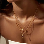 Close-up of the Embrace Change Garnet Lotus Triple Necklace worn by a model, highlighting the intricate details of the garnet teardrop and lotus pendant against a sun-kissed skin tone. This beautifully crafted talisman serves as a protective element and symbolizes love, making it a perfect accessory for yoga, spiritual growth, and self-expression.