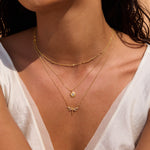 Gold-toned layered necklaces with sun and dragonfly pendants worn on model's neck.