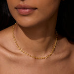 A close-up of a model wearing the Golden Hour Coin Chain Necklace, showcasing its elegant 16" length with a 3" extender. This stylish piece of spiritual jewelry enhances your yoga practice, representing the sun and moon's balance in spiritual meaning and manifestation.