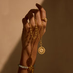 A hand adorned with the Journey to Love Rose Quartz Lotus Heart Ring, holding a gold necklace, symbolizing spiritual jewelry and meditation. This meaningful piece combines elements of the sun and moon, representing protection and love, perfect for yoga practitioners and those interested in zodiac meanings and manifestation.