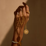 A hand adorned with the Journey to Love Rose Quartz Lotus Heart Ring, holding a gold necklace, symbolizing spiritual jewelry and meditation. This meaningful piece combines elements of the sun and moon, representing protection and love, perfect for yoga practitioners and those interested in zodiac meanings and manifestation.