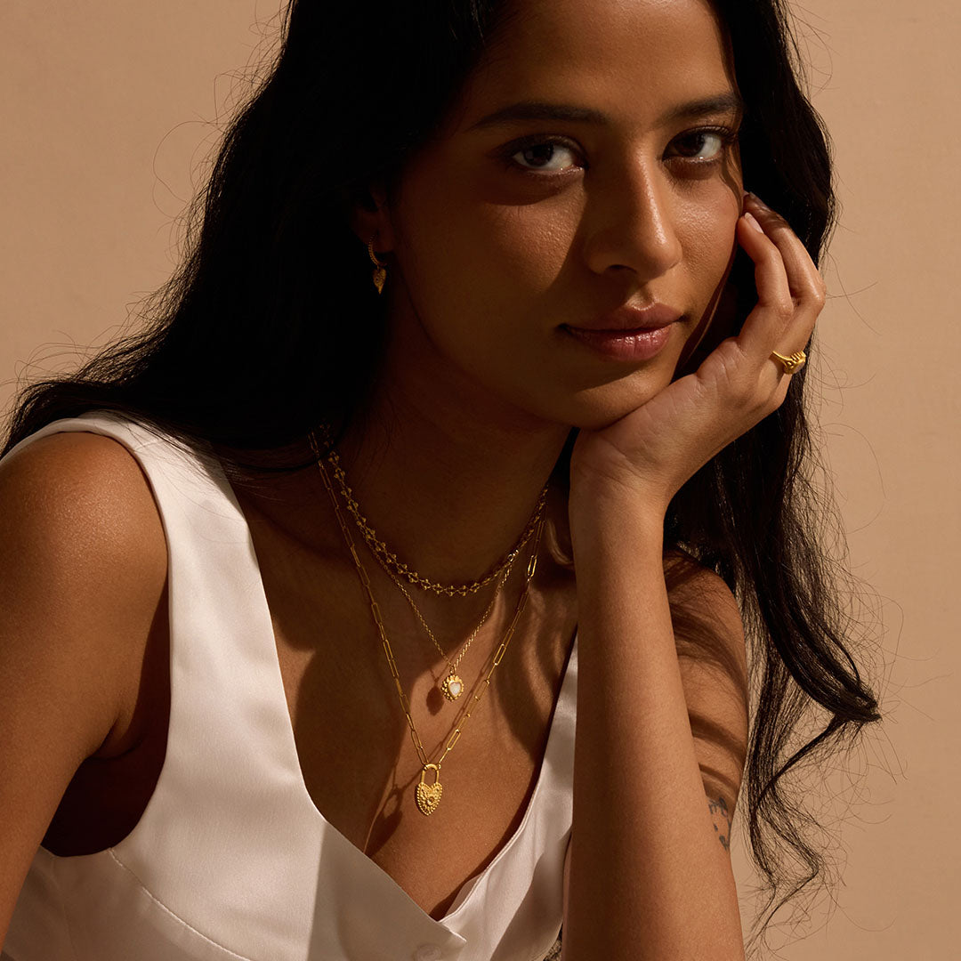 Close-up of a model wearing multiple layers of jewelry, including the Journey to Love Moonstone Lotus Heart Necklace, embodying a blend of spiritual aesthetics. This necklace serves as a talisman for those interested in yoga and zodiac meanings, enhancing spiritual connections and manifestations.