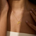 A gold chain necklace with two small textured heart pendants, each set with a tiny clear stone, rests on a person's collarbone.