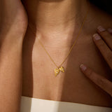 A gold chain necklace with two small textured heart pendants, each set with a tiny clear stone, rests on a person's collarbone.