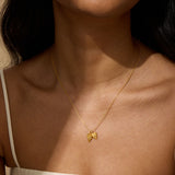 A woman wearing a thin gold chain necklace with two small heart-shaped pendants resting at her collarbone, dressed in a white strap top.