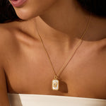 Gold chain necklace with rectangular mother of pearl pendant featuring a sun design worn on bare skin.