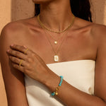 Gold layered necklaces with mother of pearl sun pendant and rectangular charm worn on person's chest.