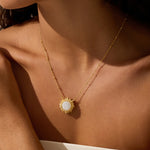 Gold-tone necklace with white moonstone pendant surrounded by radiating sun-ray details worn on bare skin.