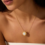 Gold-toned necklace with a sun-shaped pendant featuring a white moonstone center, worn on a person's chest.