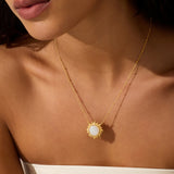 Gold-toned necklace with a sun-shaped pendant featuring a white moonstone center, worn on a person's chest.