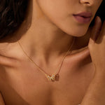 Gold-toned necklace with delicate butterfly pendant worn on model's chest.