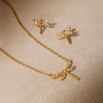 Gold-tone dragonfly necklace and matching stud earrings with white crystal accents on beige background.