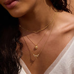 Gold chain necklace with dragonfly pendant and white topaz stones, worn layered on model's neck.