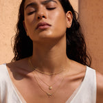 Gold-toned layered necklace with dragonfly and star pendants worn on person with white top.