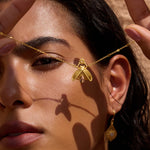 Gold-toned firefly pendant necklace with textured wings worn on model's face.
