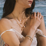 Gold-toned chain necklace with opal conch shell pendant worn layered at various lengths on a person near water.
