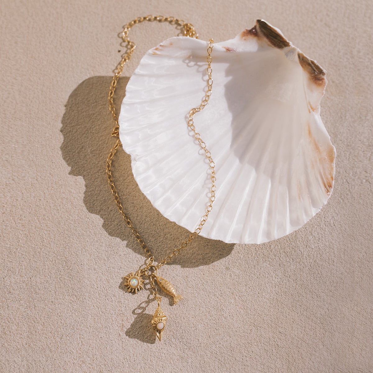 Gold chain necklace with white shell pendant and small gold charms including a sun motif and shell designs.