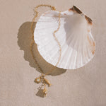 Gold chain necklace with white shell pendant and small gold charms including a sun motif and shell designs.