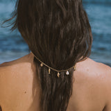 Gold chain necklace with shell and pearl charms worn around braided dark hair at the beach.