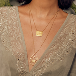 A close-up of the Sacred Commencement Lotus Necklace, showcasing the square pendant with an engraved lotus design, symbolizing spiritual growth and meaningful connections in a serene setting.