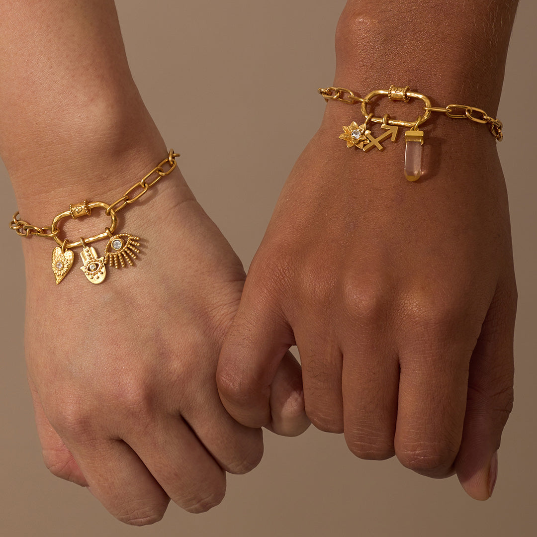 Gold-tone chain bracelet with lotus flower charm, winged pendant, and crystal drop worn on wrist.