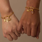Gold-tone chain bracelet with lotus flower charm, winged pendant, and crystal drop worn on wrist.