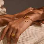A close-up of a hand wearing the Infinite Possibilities Moonstone Celestial Charm on a bracelet, showcasing its 18kt gold plating and crescent moon design. This spiritual jewelry piece symbolizes meditation and manifestation, making it a meaningful talisman for those who seek protection and guidance from the sun and moon in their yoga practice.