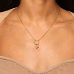 Model wearing the Universal Om White Topaz Charm on a delicate gold chain necklace. This meaningful piece of spiritual jewelry embodies the essence of the sun and moon, ideal for those seeking a talisman for protection and inspiration during yoga and meditation.