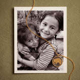 A gold chain necklace with a round elephant pendant lies across a black-and-white print of two smiling, embracing children.