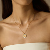 A woman wears a thin gold chain necklace with a round pendant featuring a gold elephant on a pale background.