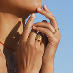 Gold stacked ring with colorful gemstone accents worn on model's hand against blue sky.